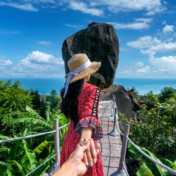 Women tourists holding man's hand and leading him to overlap stone at Koh Samui, Thailand.